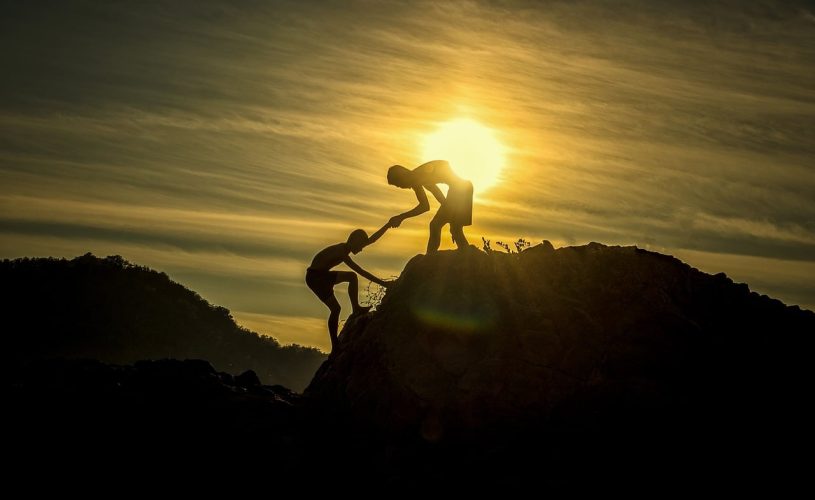 Person helping another up a mountain